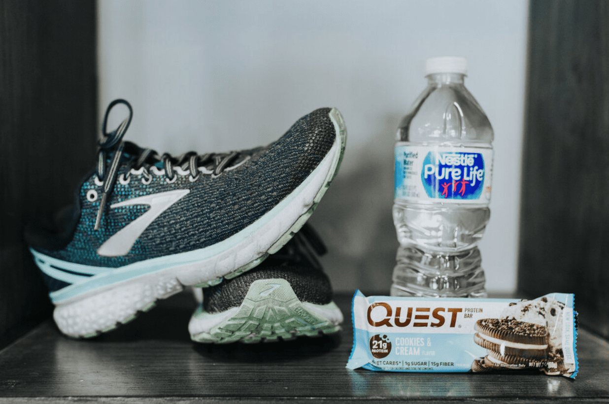 A running shoe, water bottle and Quest protein bar on a black surface